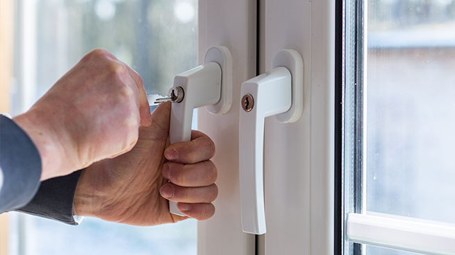 Eine Person öffnet einen abschließbaren Fenstergriff mit einem Schlüssel