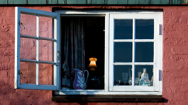 Ein nach außen geöffnetes weißes Dänisches Fenster mit Sprossen in einer roten Hausfassade