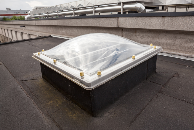 transparente Lichtkuppel auf einem Industriegebäudedach mit Rohren im Hintergrund
