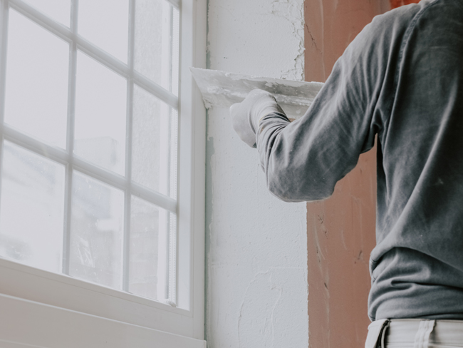 Eine Person verputzt die Fensterlaibung