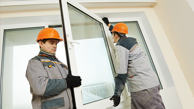 Zwei Handwerker bauen ein Fenster ein und tauschen gerade den Flügel