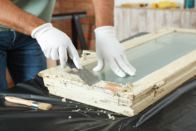 Handwerker setzt altes Holzfenster instand und entfernt Farbe vom Rahmen