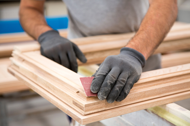 Tischler schleift den Flügel eines Holzfensters mit der Hand ab