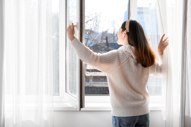 Frau öffnet Fenster um mal richtig zu lüften