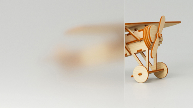 Ein Spielzeugflugzeug aus Holz hinter einer Glasscheibe aus Satinato Glas