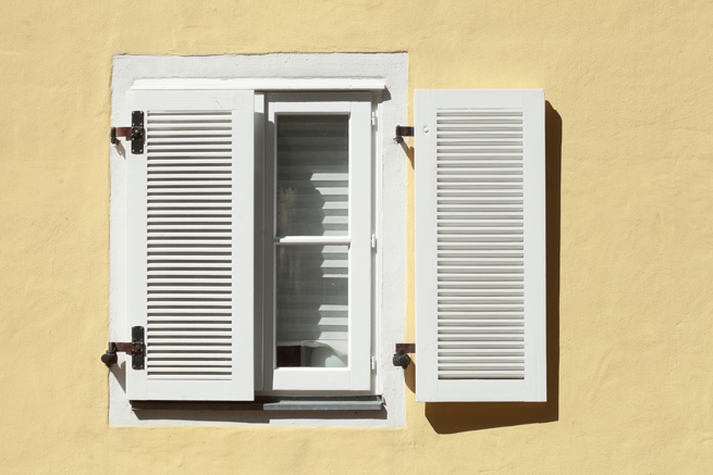 Weiße Fensterläden als Sonnenschutz vor Holzfenster