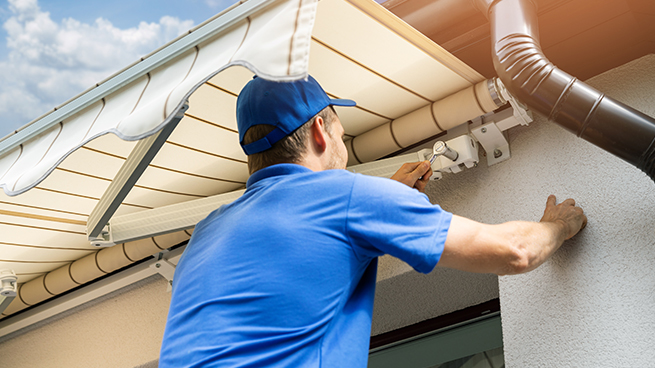 Mann kontrolliert die Technik einer Markise am Haus