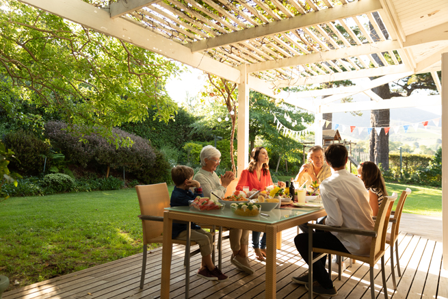 Familie sitzt unter einer Terrassenüberdachung und genießt den Sommer im Garten