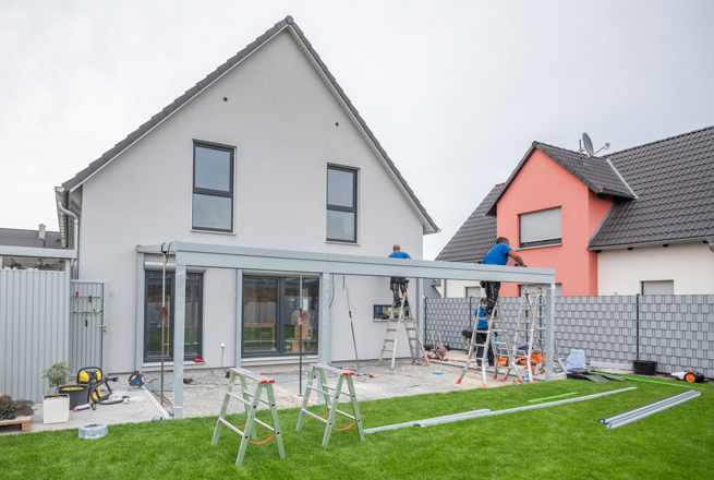 Rückseite Wohnhaus mit einem Team welches gerade eine Terrassenüberdachung aufbaut
