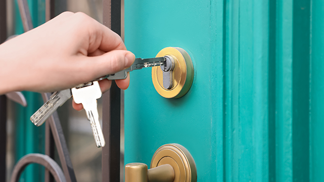 Main féminine déverrouille la serrure cylindrique d'une porte d'entrée vert menthe