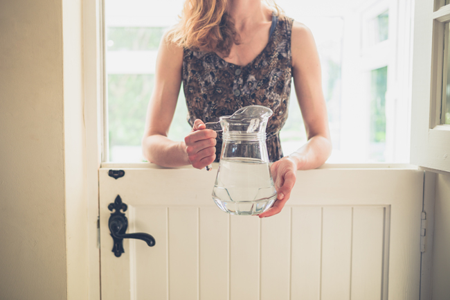 Eine Frau hält einen Wasserkrug und steht vor der halb geöffneten Klöntür