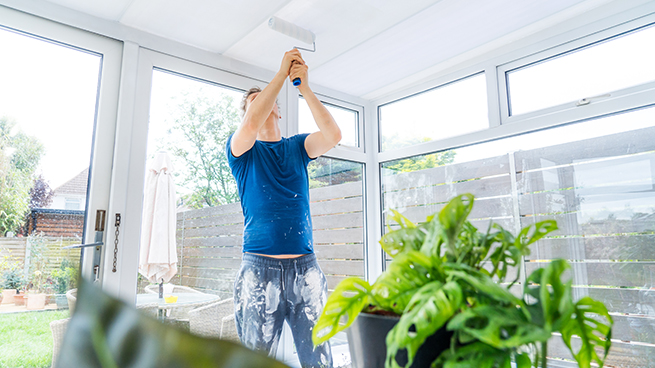 Mann walzt mit einer Farbwalze die Decke eines Wintergartens