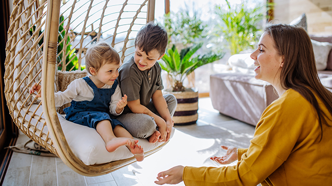 Spielende Kinder mit ihrer Mutter in einem Hängekorb im Wintergarten des Hauses