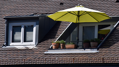 Dachbalkon mit gelbem Sonnenschirm neben einem Kunststofffenster in einer Dachgaube