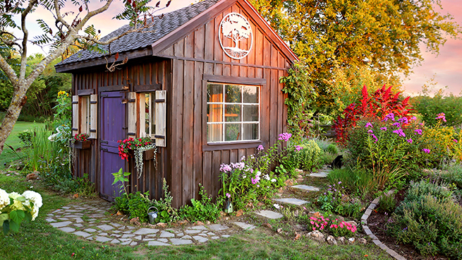Gartenhäusschen in einem blühenden Garten im Schein der Abendsonne mit weißen Holzfenstern