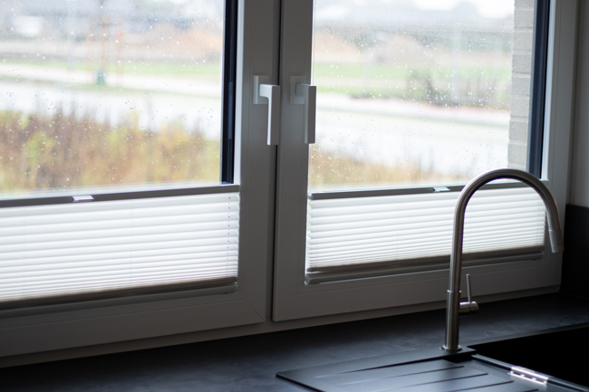 Zweiflügeliges Küchenfenster mit Plissees hinter Spüle
