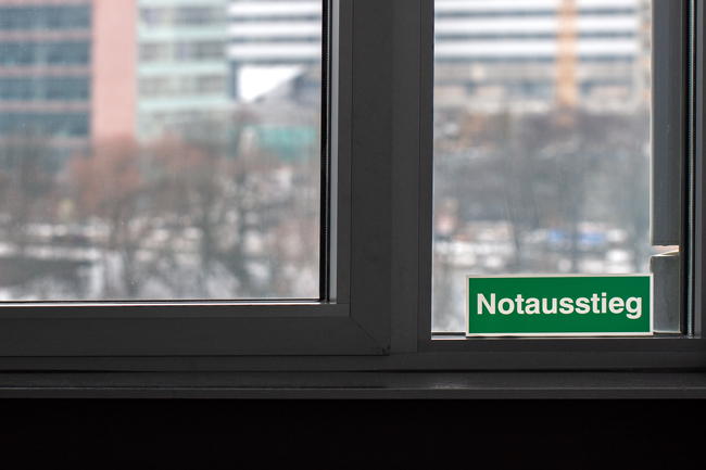 Ein geschlossenes weißes Notausstiegsfenster mit einem auffälligen grünen Hinweisschild am Rahmen