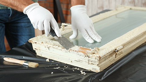 Rénover de vieilles fenêtres : Un artisan enlève l'ancienne peinture de la fenêtre en bois