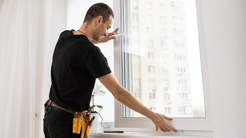 Un homme devant une fenêtre vérifie pourquoi une fenêtre ne se ferme pas correctement