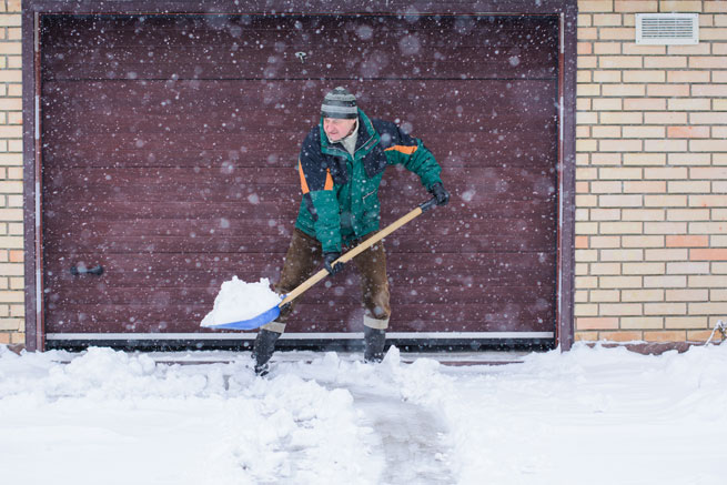 Homme poussant de la neige devant le garage
