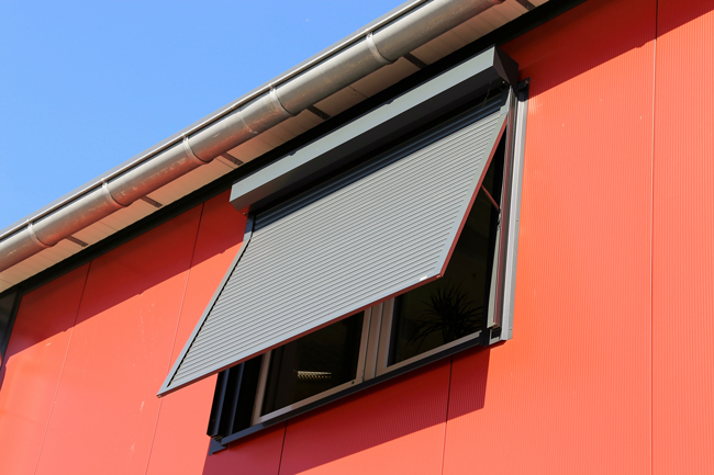 Eine Fenstermarkise in Anthrazit vor einem Fenster in einer roten Hausfassade