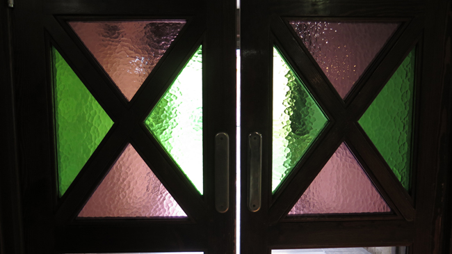 Zweiflügelige Pendeltür mit Glaseinsätzen aus rosa und grünem eingefärbtem Glas