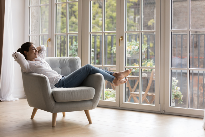 Frau relaxed auf einem Sessel im Wohnzimmer mit Blick durch die Kunststofffenster Wand