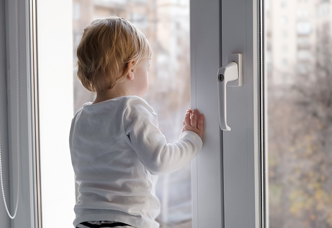 Kleinkind steht sicher an Kunststofffenster neben eine abschließbaren Fenstergriff