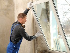 Un artisan installe une fenêtre en PVC de l'intérieur dans un mur d'un ancien bâtiment