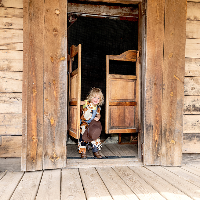 Kind steht als Cowboy verkleidet in der Schwingtüre eines Saloons